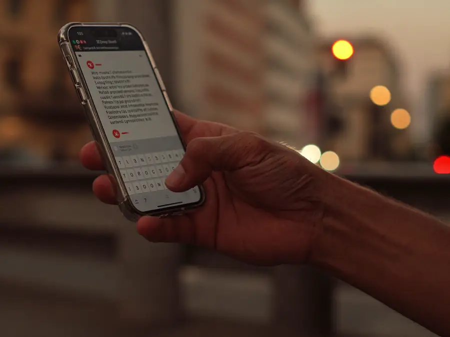Mãos digitando uma mensagem no celular numa rua ao entardecer
